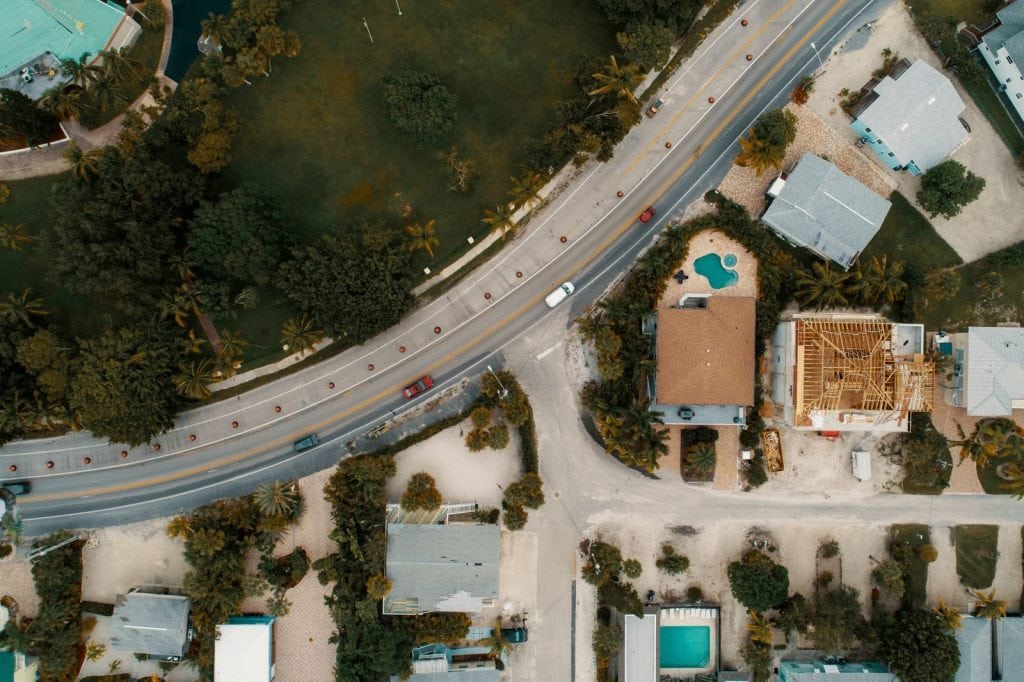 Drone view of suburban houses, road, and lush greenery, showcasing modern architecture.