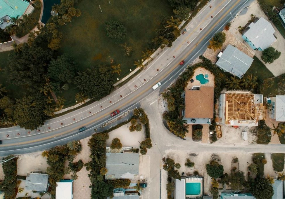 Drone view of suburban houses, road, and lush greenery, showcasing modern architecture.