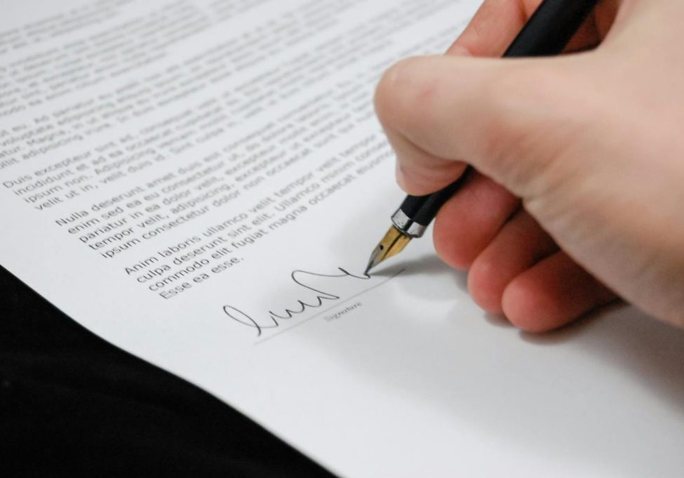 Close-up of a hand signing a legal document with a fountain pen, symbolizing signature and agreement.